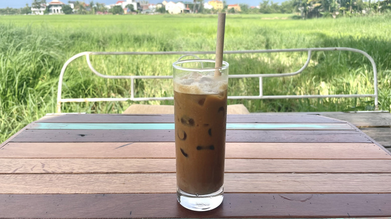 Cafe sua glass with straw sitting on wooden table overlooking rice paddies