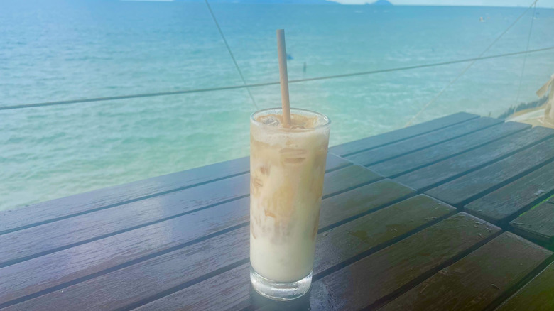 Yogurt coffee glass with straw sits on wooden table overlooking the sea