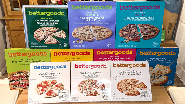 Ten flavors of bettergoods brand frozen pizzas displayed on a table