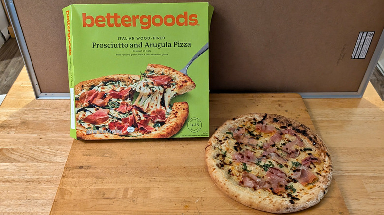 A freshly cooked bettergoods wood-fired prosciutto and arugula pizza beside the box it came in