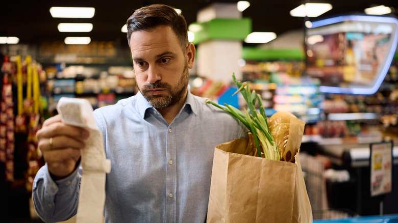A man reflecting on the cost of his groceries while looking at his reciept