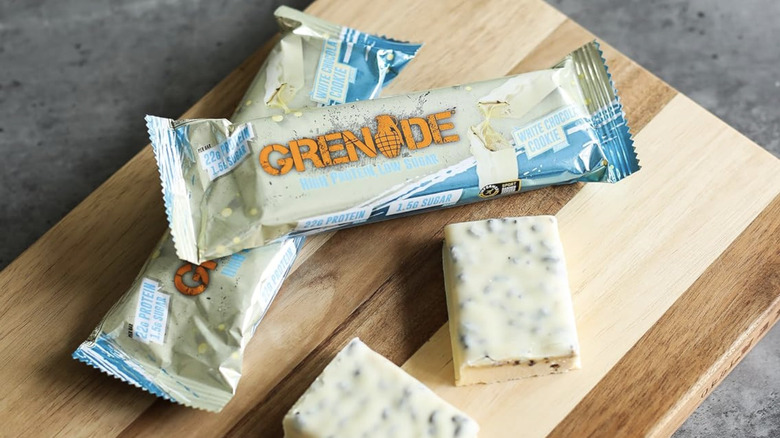 Wrapped and unwrapped Grenade white chocolate bars on a wooden chopping board.