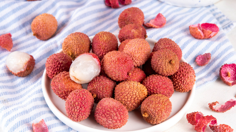 Fresh raw ripe lychee fruits, whole, peeled, and cut, on plate