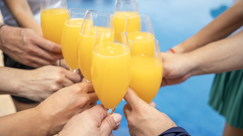 Multiple people toast with mimosas in champagne flutes by the pool
