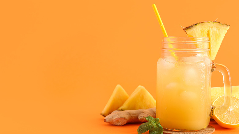 Mason jar of fresh pineapple juice with mint and ginger root on orange background