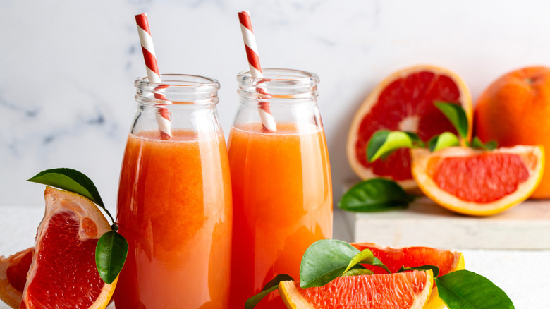 Freshly made grapefruit juice in glass bottles next to slices of the fruit
