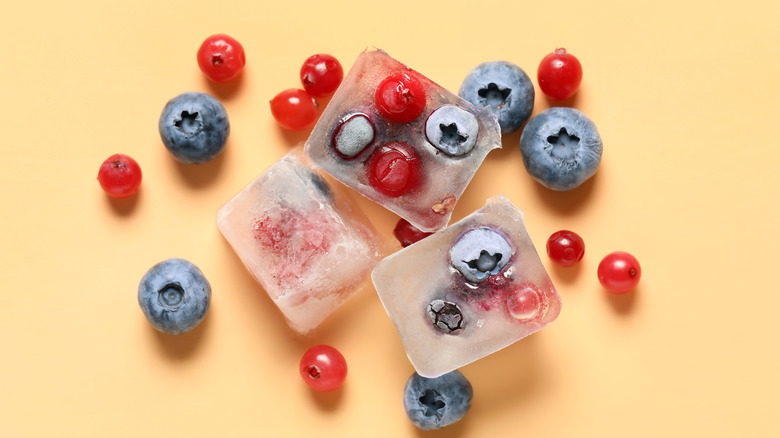Frozen blueberries and cranberries in ice cubes on orange background