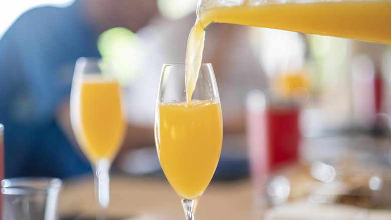 Mimosa poured from pitcher into champagne flute on restaurant table