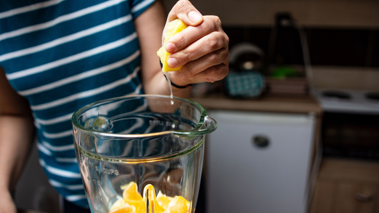 Close-up of female hands squeezing oranges into blender for natural juice