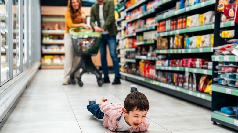 Shot of small boy lying on floor and fusses while his mom and dad shops for groceries