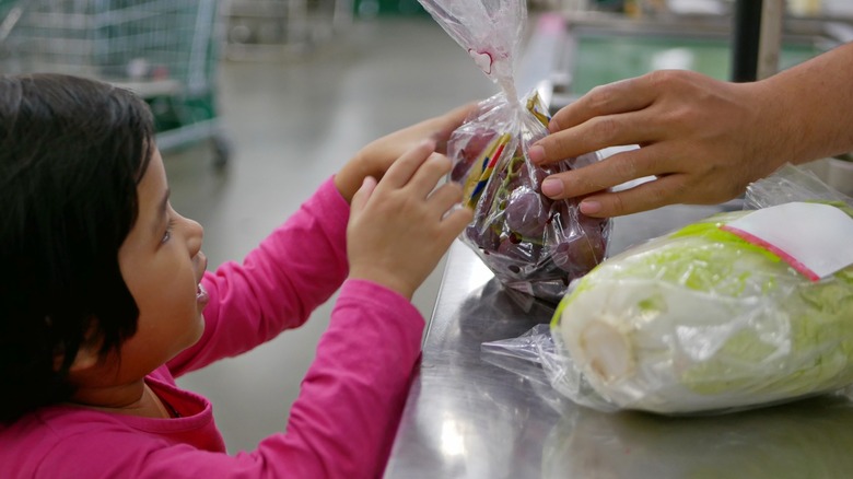 little girl handing cashier clerk grocery item
