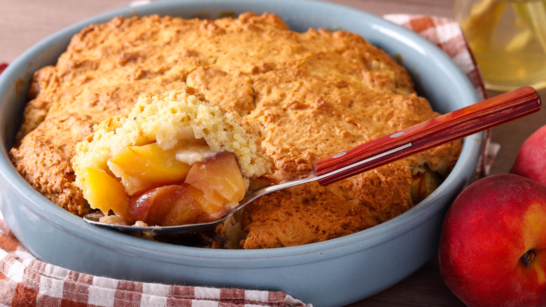 Homemade warm peach cobbler in a tin with a spoon tucked into it