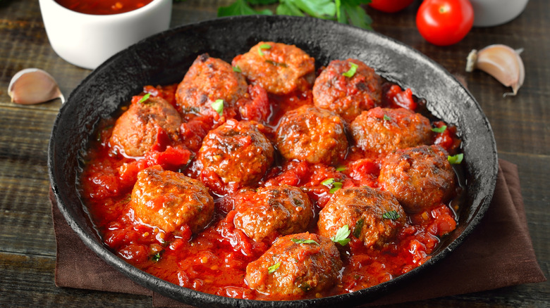 Delicious homemade meatballs in a tomato-baed sauce in a black bowl garnished with fresh parsley