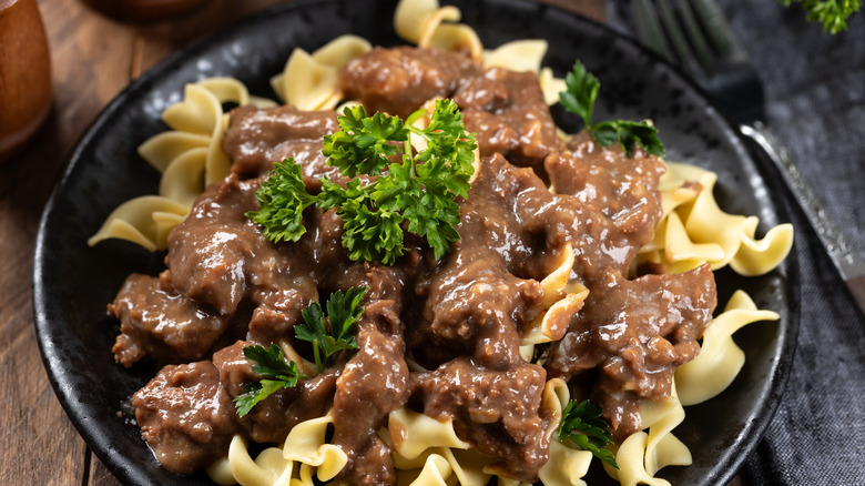 Beef stroganoff with egg noodles garnished with parsley on a black dinner plate