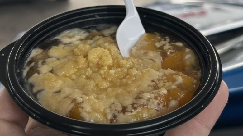 A hand holding a container of Buc-ee's peach cobbler