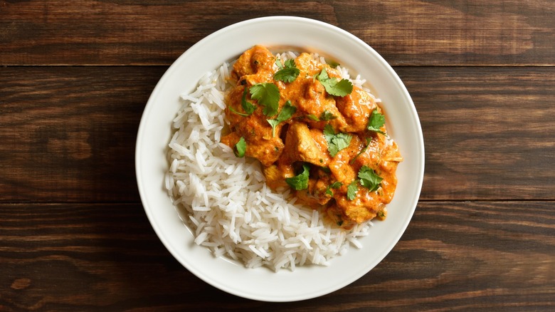Butter chicken with basmati rice on white plate on wooden background
