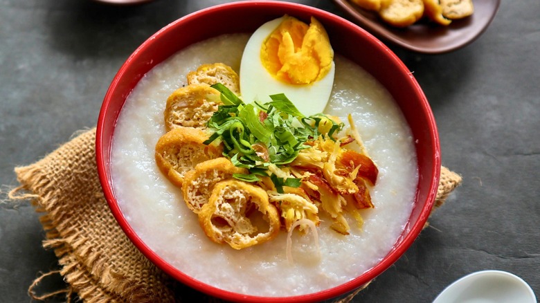 A close-up overhead view of a steaming bowl of congee, garnished with a hard-boiled egg and golden fried dough pieces