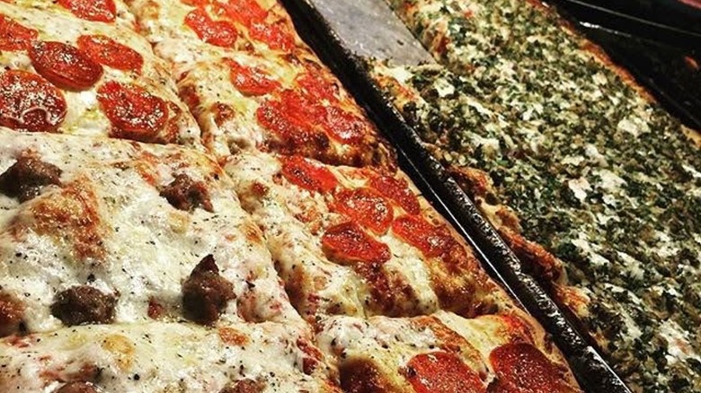 Various rectangular slices of pizza on metal trays, including pepperoni and sausage at Golden Boy Pizza restaurant