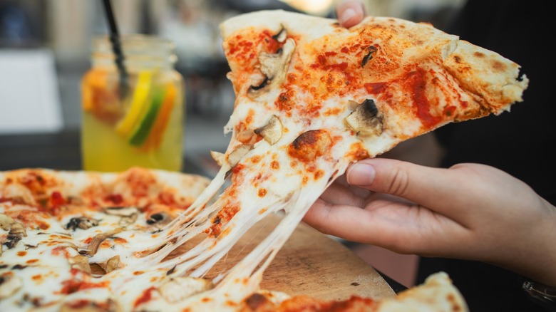 Close-up of a hand taking a slice of mushroom pizza with stretching cheese in a pizzeria restaurant