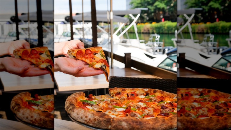 Hand holding up a slice of pizza, pulling it from a whole pizza on dockside table at Robert's Pizza & Dough Co.