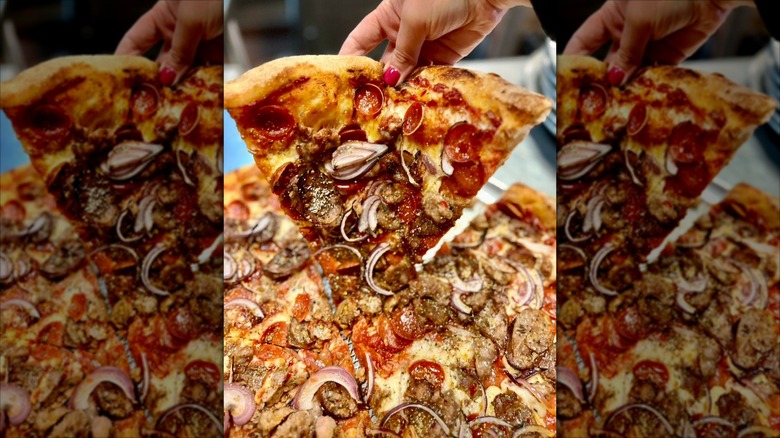 hand holding up a slice of pizza with red onions, sausage, and pepperoni from Tony's Pizza Napoletana