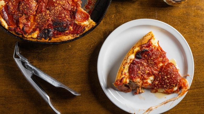 A slice of deep dish Chicago-style pizza rests on a plate with the rest of the pie in a pan
