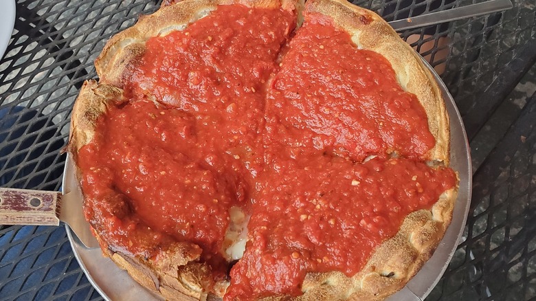 A birds eye view of a Chicago-style pizza from Carmines on a metal table outside