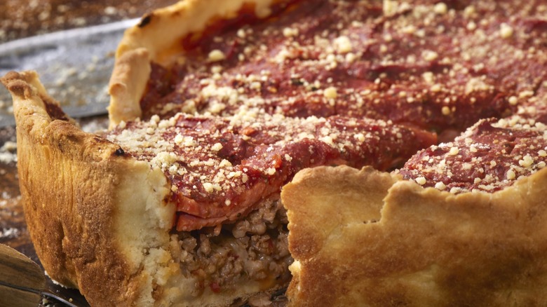 A Chicago-style pizza with a slice being lifted from the pie on a pie server