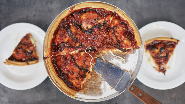 A Chicago-style pizza rests in the middle, a slice on each plate to the left and right of it