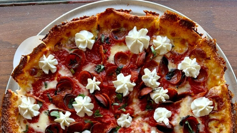 A deep dish Chicago-style pizza resting on a table with peperoni and ricotta dollops