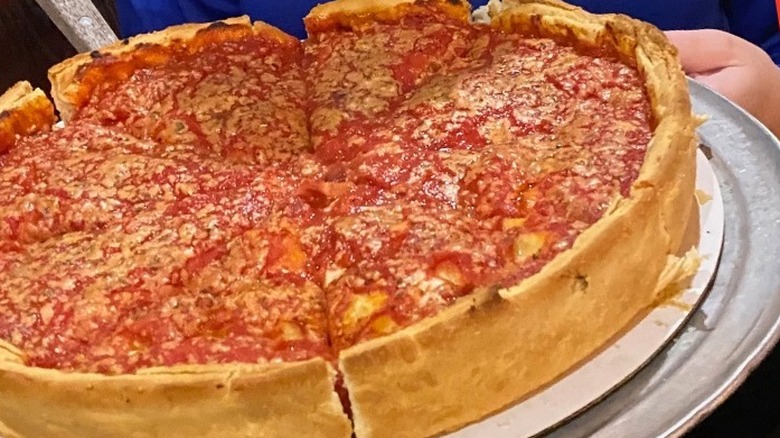 A Chicago-style pizza rests on a metal pan held in the arms of a waitress at the Wig and Pen pub