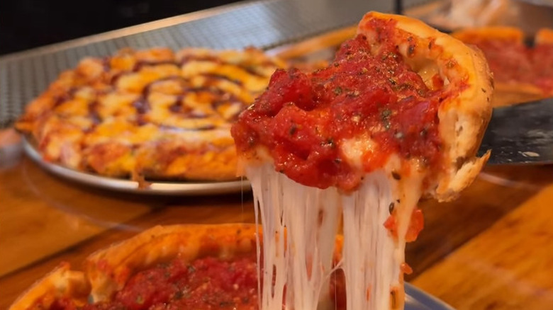 A slice of Chicago style pizza is being lifted from the pie below attached by several strings of cheese