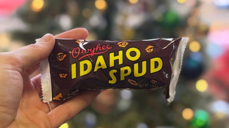 A hand holding an Idaho Spud Candy Bar against a blurred backdrop of Christmas lights