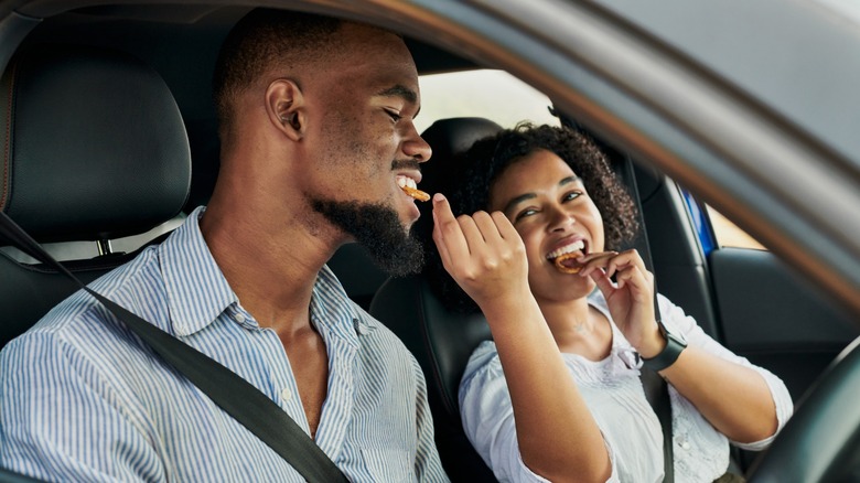 A couple on a road trip, smiling while sharing snacks in the car