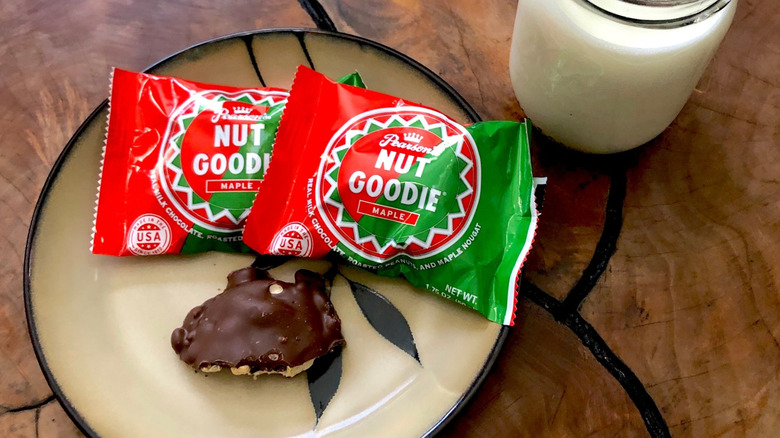 Two packages of Nut Goodie candy and a single half-eaten Nut Goodie on a plate next to a glass of milk