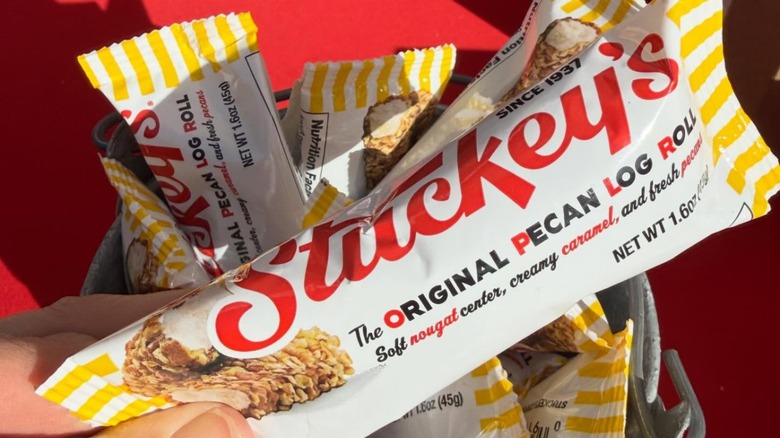 Close-up of a hand holding a package of Stuckey's Pecan Log Roll over a red surface