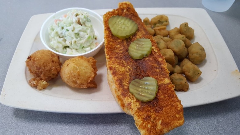 A piece of Captain D's Nashville Hot Fish on a platter, covered with pickles with hush puppies, fried okra, and cole slaw.