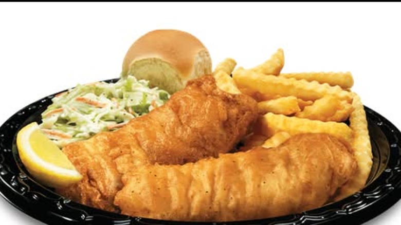 Culver's dinner with two pieces of fried fish, French fries, cole slaw, a roll, and a lemon wedge on a black plate.
