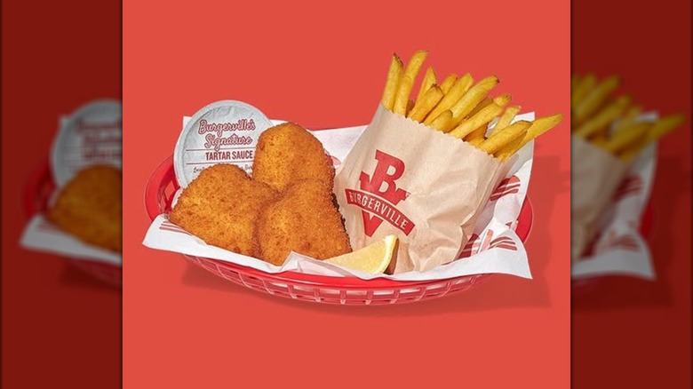 Three pieces of Burgerville wild caught fish with fries, tartar sauce and a lemon wedge in a basket on a red background.