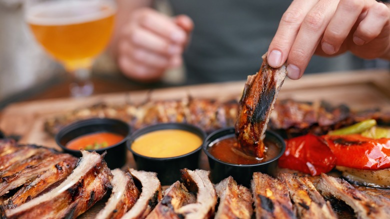 Hand dipping section of barbecue rib into sauce on platter with Barbecue Ribs and Sauсes next to glass of beer