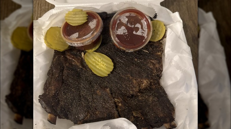 BBQ ribs with side sauce and pickles in to go container from Ooh Wee Bar-B-Q
