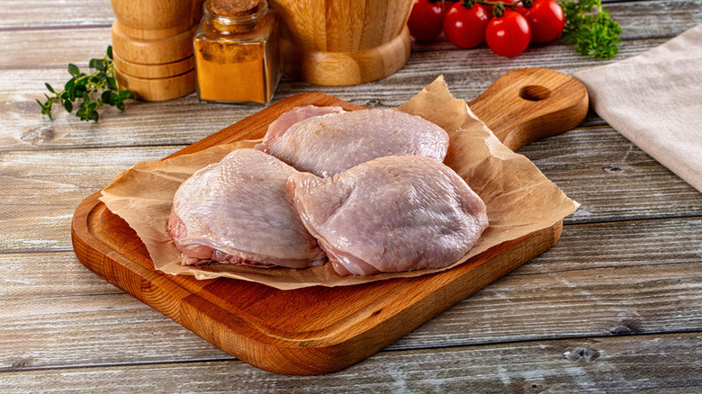 Raw chicken thighs for cooking over wooden cutting board lined with butcher paper