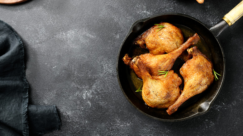 Duck legs confit in a cast iron pan garnished with rosemary sprigs