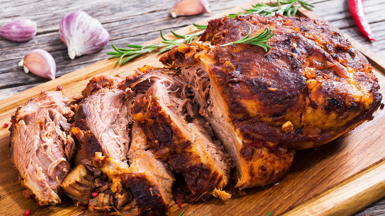 Big Piece of Slow Cooked Pulled Pork shoulder on chopping board with mixed peppercorns, rosemary, and garlic