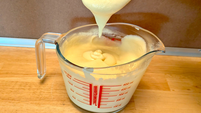 A microwaved dessert custard in a measuring cup with a spoon of custard dripping into the cup