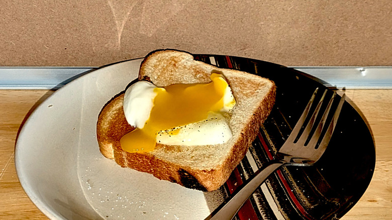 A microwaved poached egg on a plate cut open so the runny yolk is visible on a piece of toast