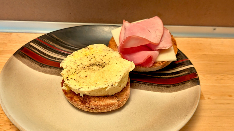 A fluffy microwaved egg patty on an English muffin topped with ham and cheddar cheese