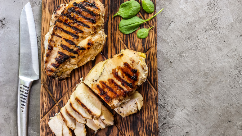 Grilled whole and sliced chicken breasts on wooden cutting board