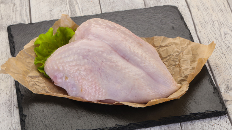 Whole raw bone-in skin-on chicken breast on piece of parchment paper