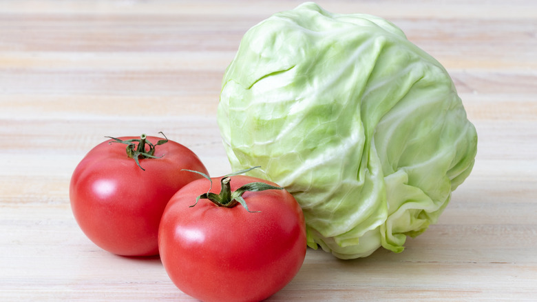 Raw cabbage and two tomatoes on a wood table